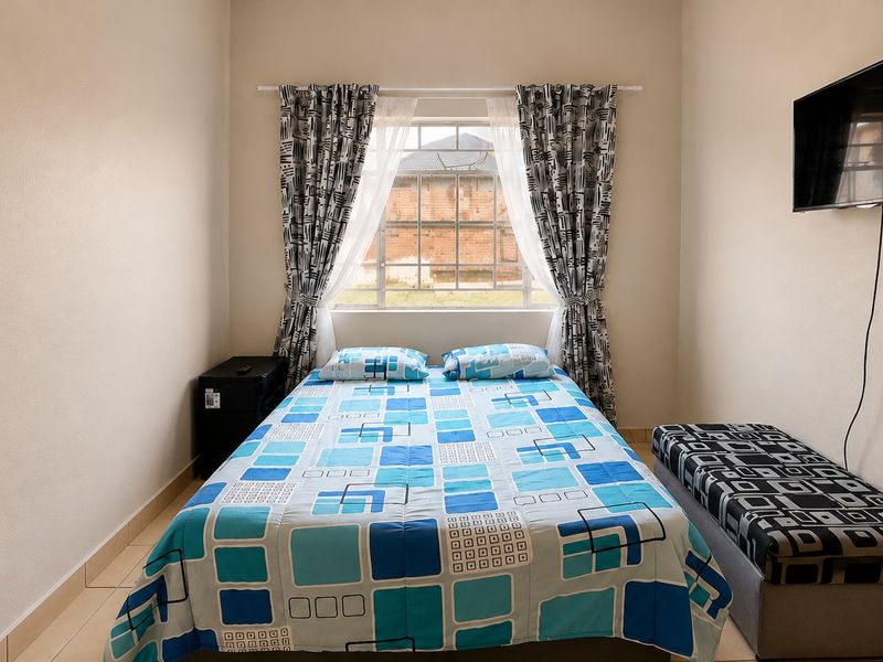 A functional bedroom featuring tiled flooring, a central window, and wall-mounted television space.