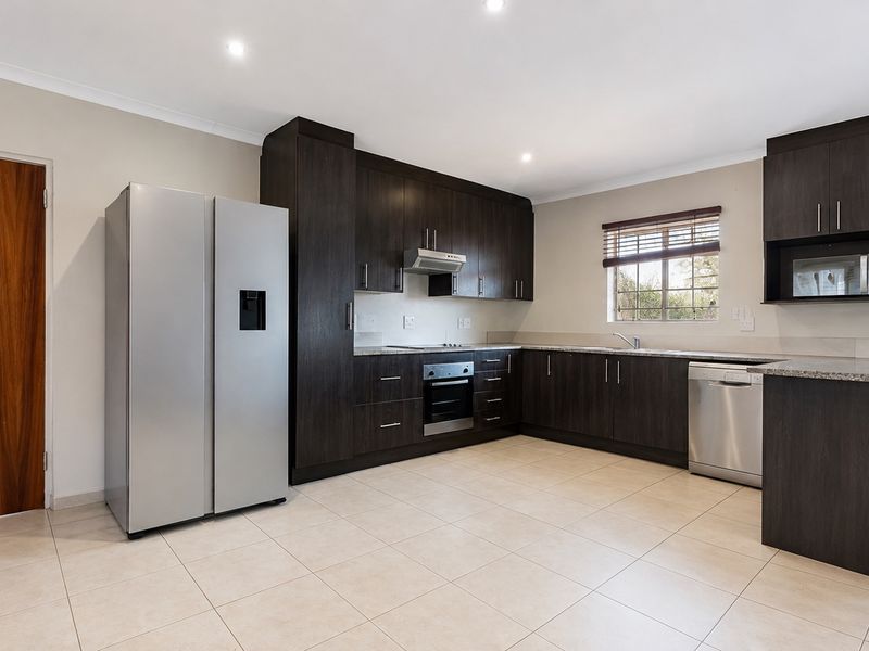 Modern kitchen featuring dark wood cabinetry, granite countertops, built-in oven, extractor fan, and tiled flooring in a clean, well-maintained space.