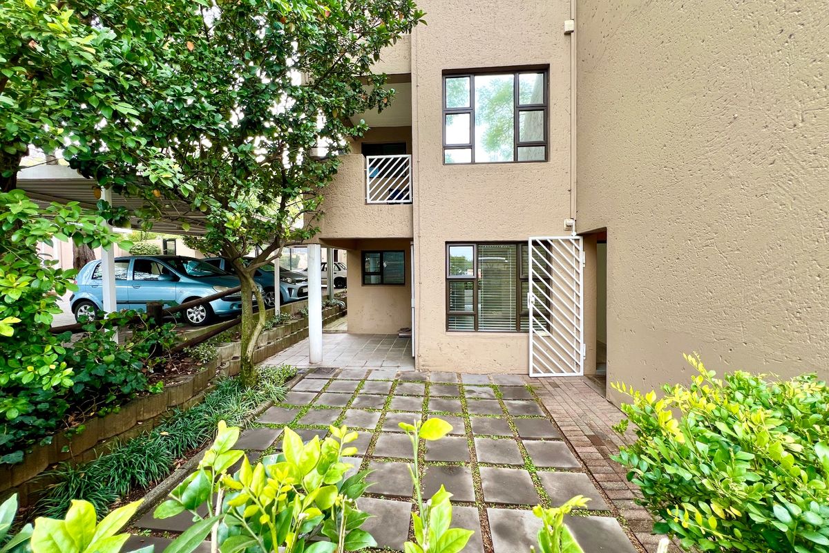 Rear exterior view of the apartment building featuring a paved patio area, security gates, and established garden landscaping.
