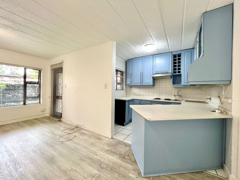 Open-plan living area featuring a kitchen with blue cabinetry, breakfast counter, and laminate flooring, leading to a bright, tiled living space.