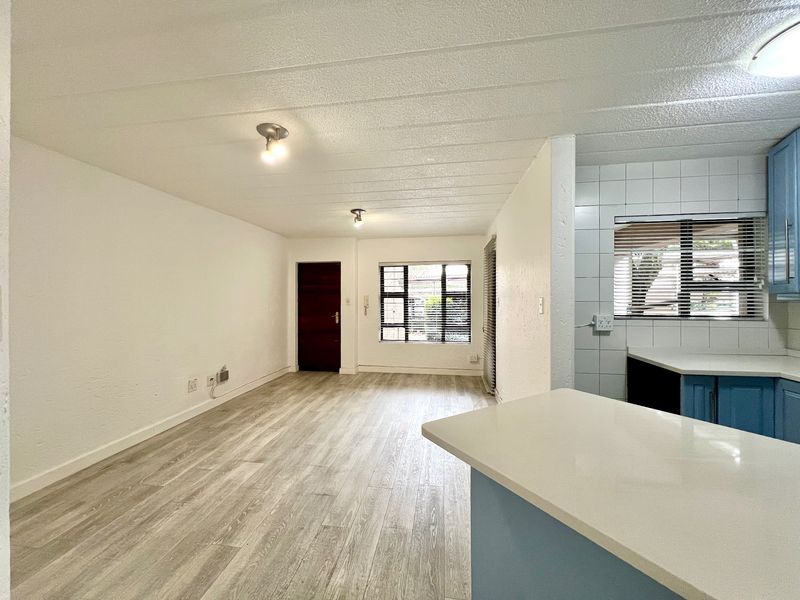 An open-plan living and kitchen area featuring light-toned laminate flooring, modern blue cabinetry, and stone countertops in a bright, vacant space.