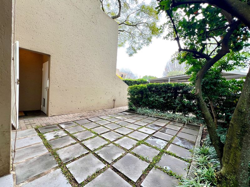 A private rear courtyard featuring a paved patio area, established garden borders, and direct access to the apartment interior.