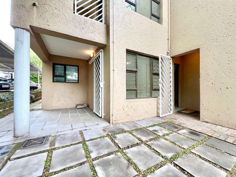 Exterior view of an apartment entrance featuring a paved patio area, security gates, and concrete paving with integrated drainage.
