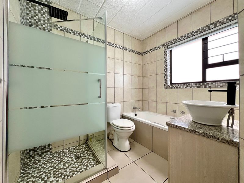 A well-maintained bathroom featuring a glass-enclosed shower, a built-in bathtub, a modern vessel sink on a granite vanity, and neutral tiled finishes.