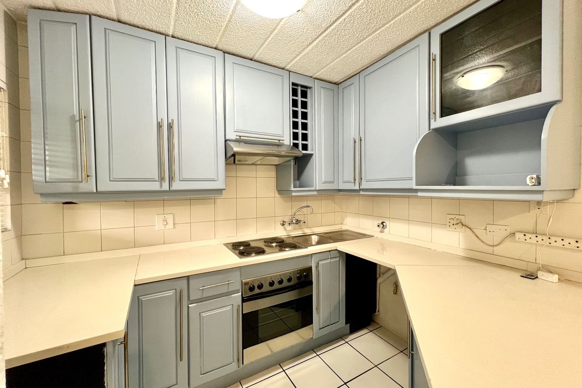 A functional kitchen featuring light blue cabinetry, built-in oven and hob, tiled backsplash, and tiled flooring, offering a clean and practical workspace.