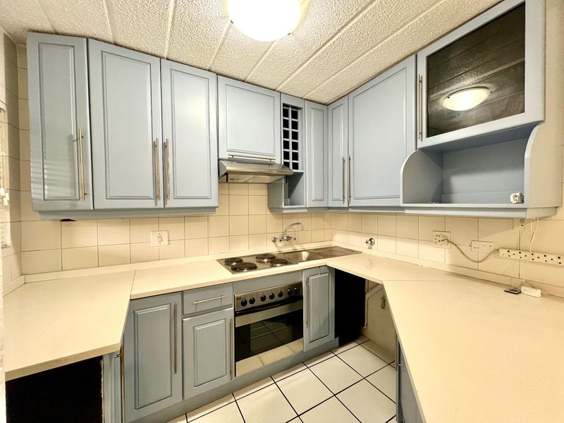 A functional kitchen featuring light blue cabinetry, built-in oven and hob, tiled backsplash, and tiled flooring, offering a clean and practical workspace.