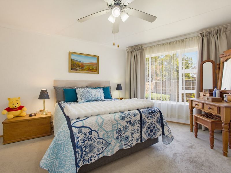 A well-lit bedroom featuring a ceiling fan, large window with natural light, and neutral carpeting, offering a comfortable and functional living space.