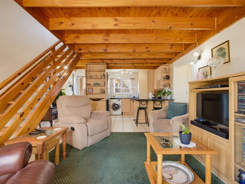 Open-plan living area featuring exposed timber ceiling beams, a wooden staircase, and an integrated kitchen with breakfast bar and tiled flooring.
