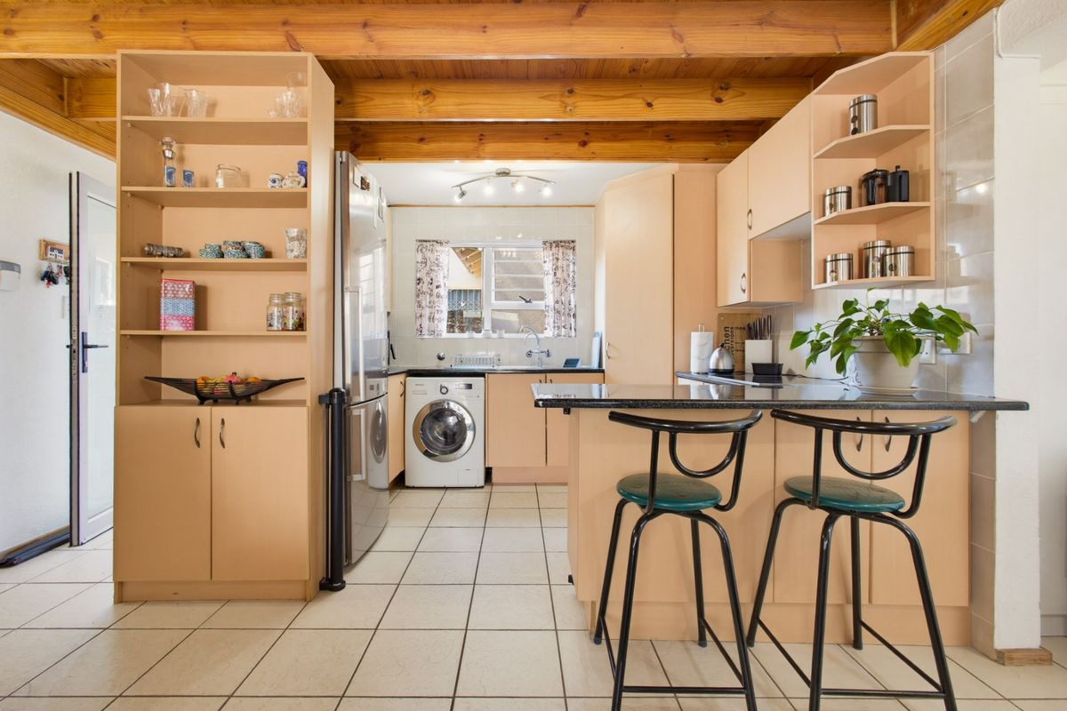 Functional kitchen featuring exposed timber ceiling beams, tiled flooring, ample built-in cabinetry, and a granite breakfast bar with integrated laundry area.