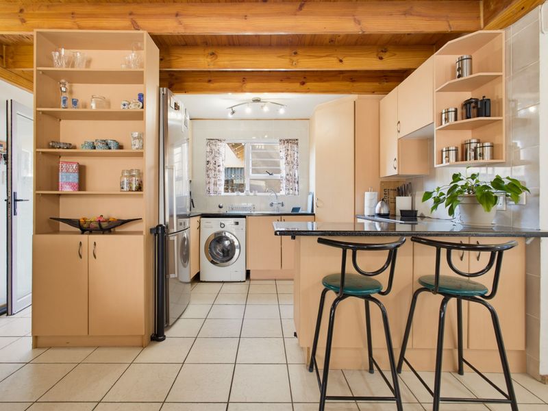 Functional kitchen featuring exposed timber ceiling beams, tiled flooring, ample built-in cabinetry, and a granite breakfast bar with integrated laundry area.