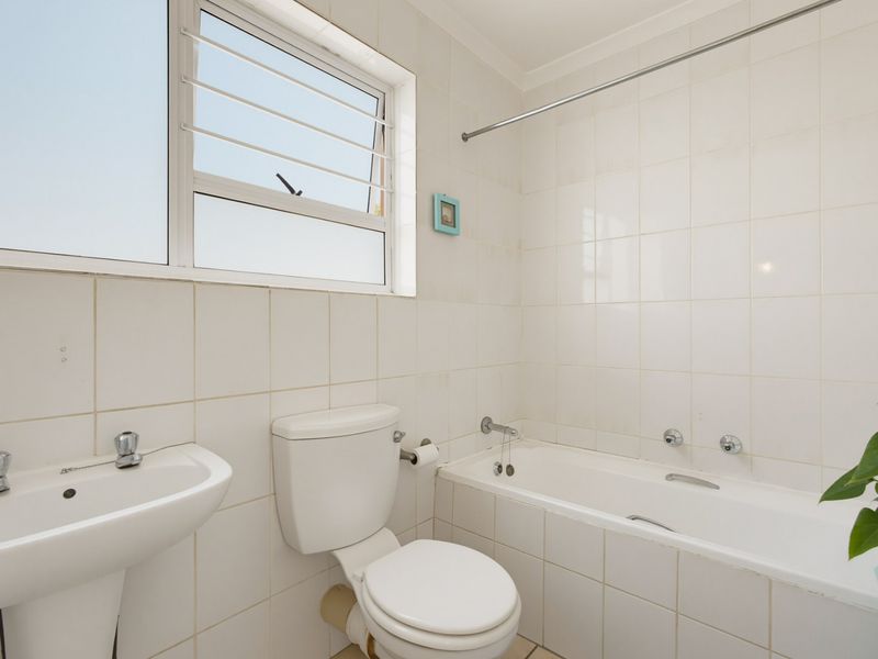A functional bathroom featuring a pedestal basin, toilet, and bathtub with tiled walls and a window for natural light.