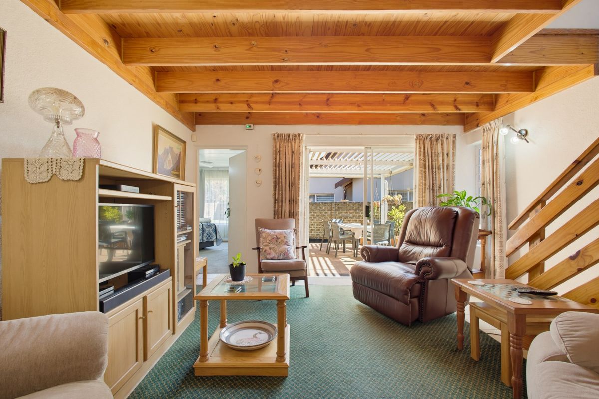Cozy living room featuring exposed timber ceiling beams, fitted carpeting, and sliding glass doors providing direct access to the outdoor patio area.