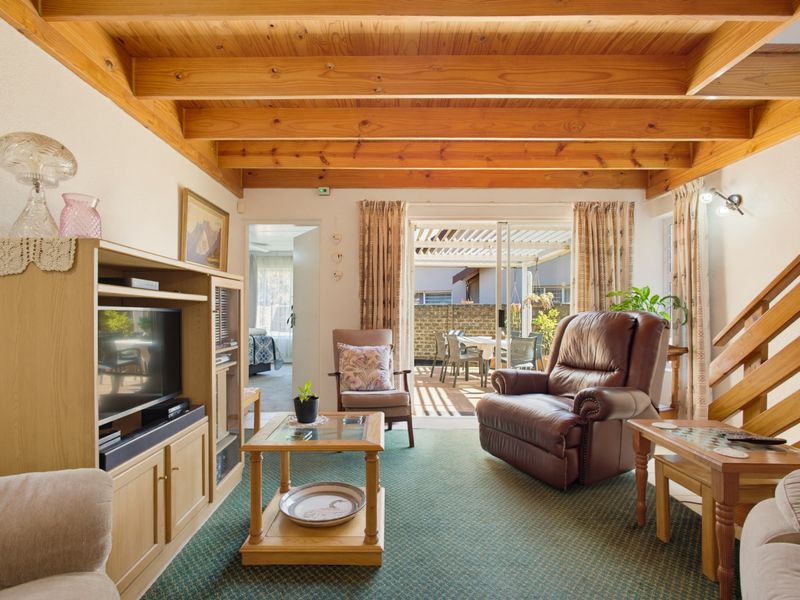 Cozy living room featuring exposed timber ceiling beams, fitted carpeting, and sliding glass doors providing direct access to the outdoor patio area.
