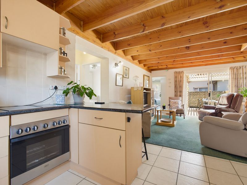 Open-plan kitchen and living area featuring exposed timber ceiling beams, tiled kitchen flooring, and direct access to an outdoor patio through sliding glass doors.