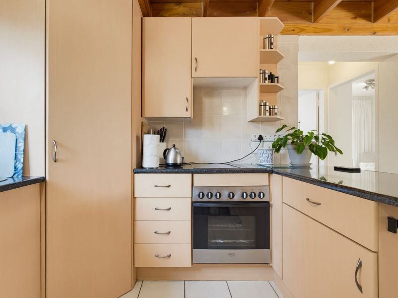 A compact kitchen featuring light-toned cabinetry, dark laminate countertops, a built-in oven with hob, and exposed timber ceiling beams.