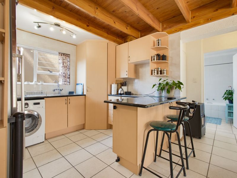 A functional kitchen featuring light laminate cabinetry, granite countertops, a breakfast bar, and exposed timber ceiling beams, with tiled flooring throughout.