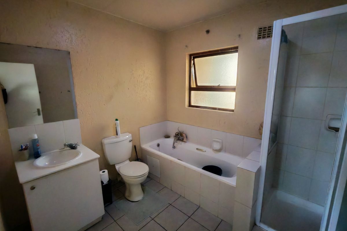 A dated bathroom featuring a vanity, toilet, bathtub, and separate shower enclosure with tiled finishes, requiring cosmetic updates to improve its overall condition.