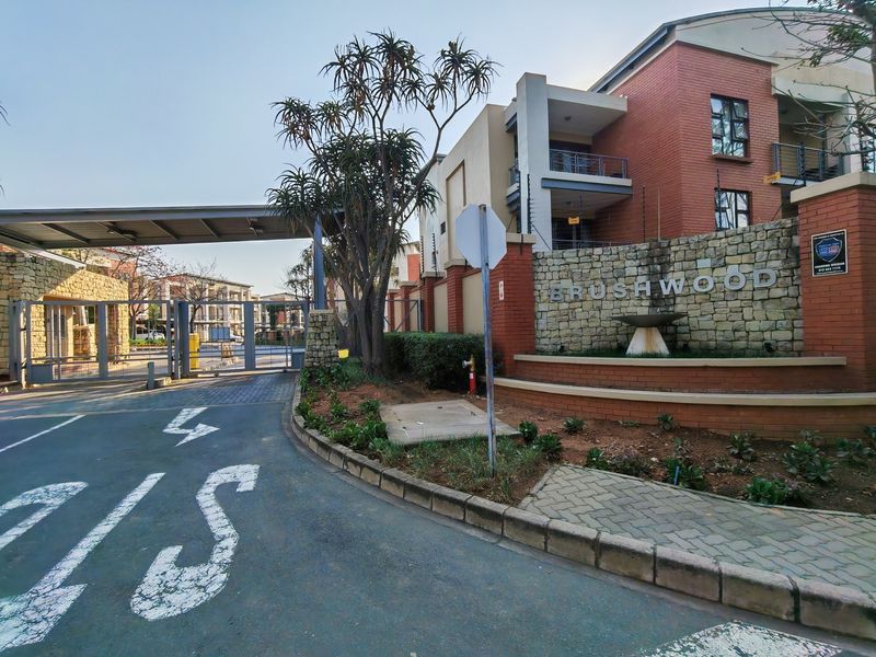 The main entrance to Brushwood apartment complex, featuring a secure gated access point, stone-clad signage wall, and well-maintained brick building facades.