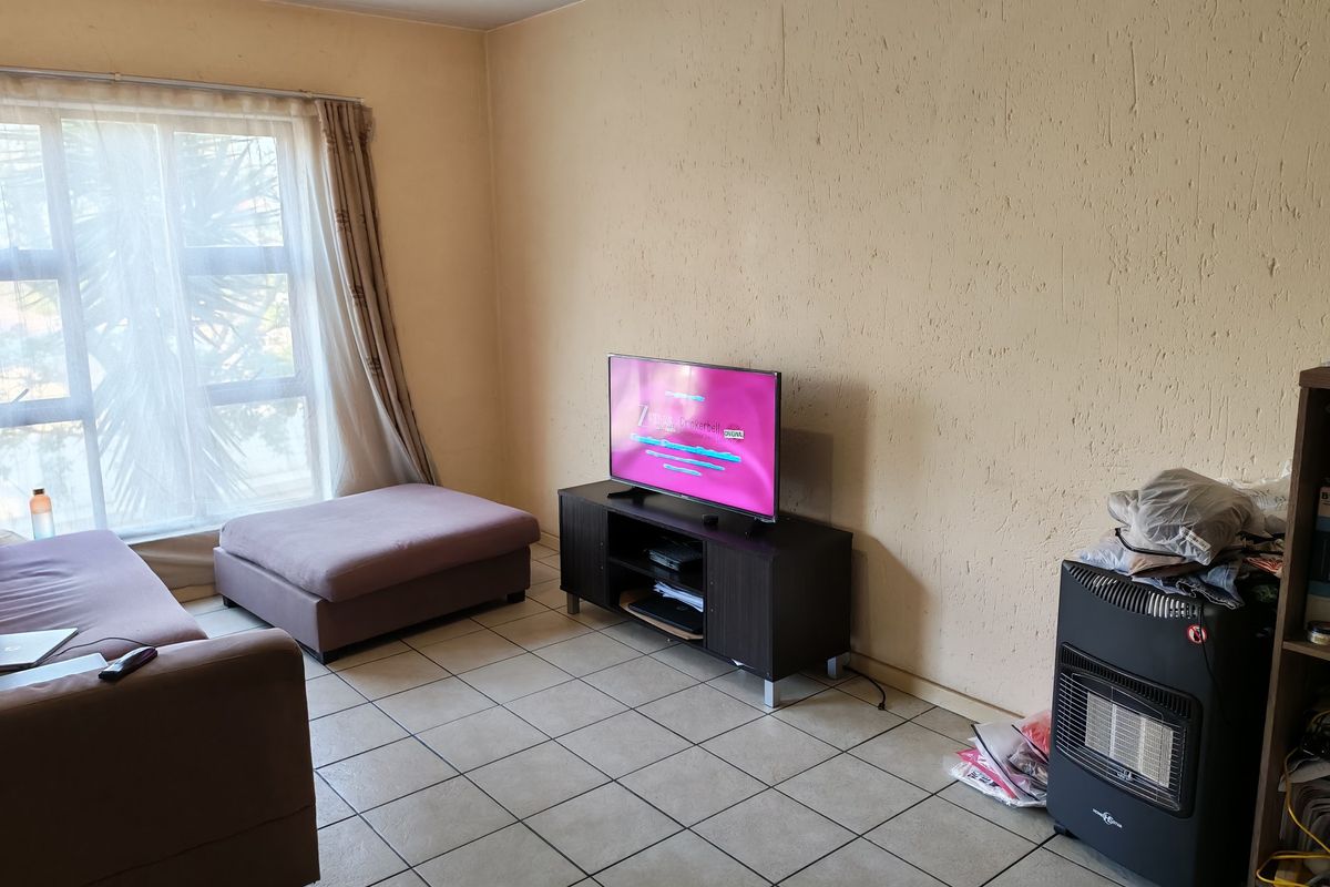 A living room area featuring tiled flooring and a large window, currently showing signs of wear on the walls.