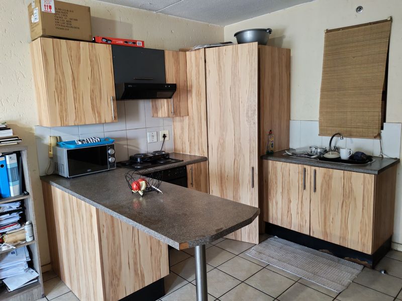Compact kitchen featuring wood-look laminate cabinetry, built-in oven and hob, and a breakfast bar counter, requiring some maintenance to base cabinetry.