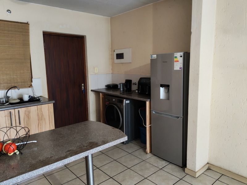 A functional kitchen area featuring tiled flooring, laminate countertops, and built-in cabinetry, providing a practical space for daily meal preparation and laundry tasks.