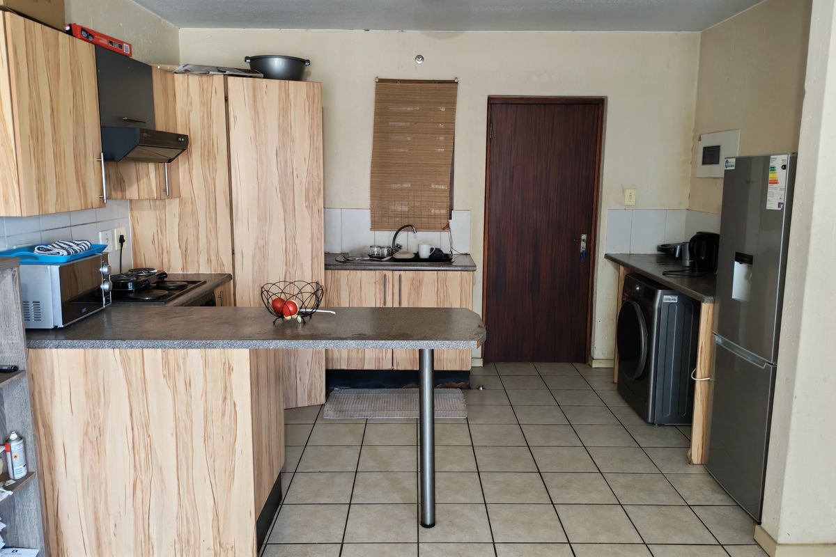 Functional kitchen featuring light wood-look cabinetry, tiled flooring, a breakfast bar, and integrated appliances, offering potential for cosmetic updates.