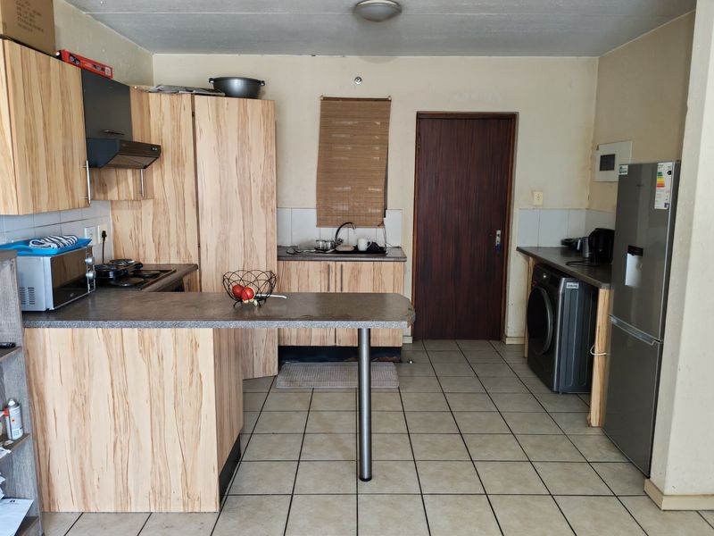 Functional kitchen featuring light wood-look cabinetry, tiled flooring, a breakfast bar, and integrated appliances, offering potential for cosmetic updates.