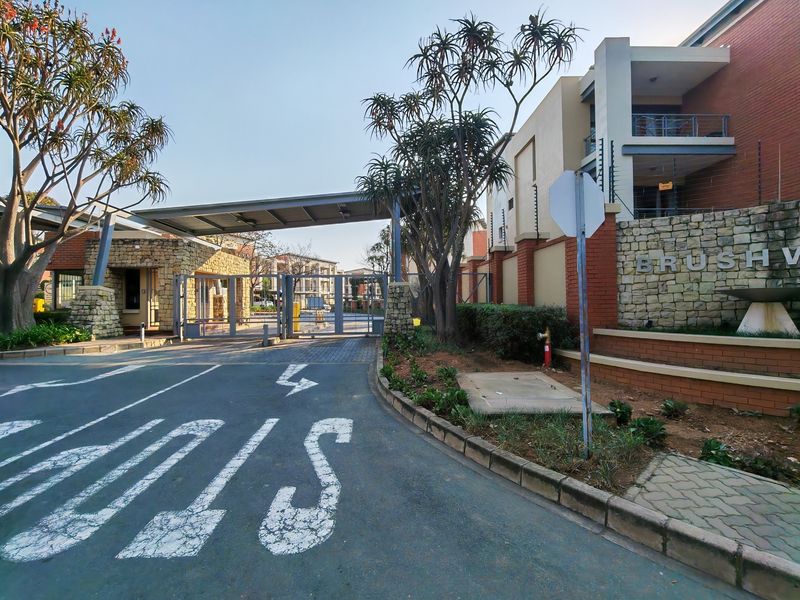 The secure entrance to the apartment complex features a gated access point, stone-clad guard house, and perimeter electric fencing.