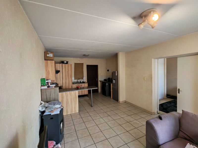 Open plan living and kitchen area featuring tiled flooring, built-in cabinetry, and a breakfast bar, requiring cosmetic updates to improve the overall aesthetic.