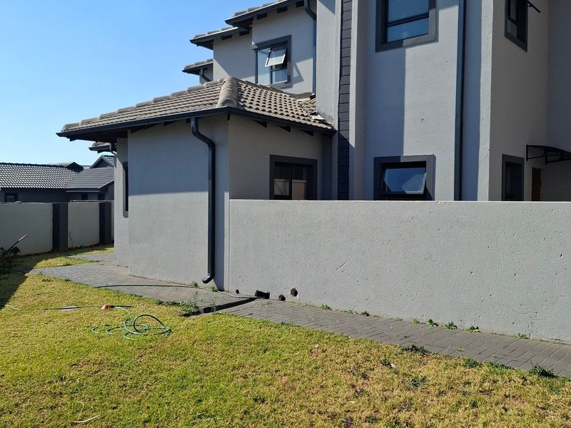 Rear view of a two-story residential house featuring a tiled roof, grey exterior walls, aluminium window frames, and a paved walkway leading to the garden.