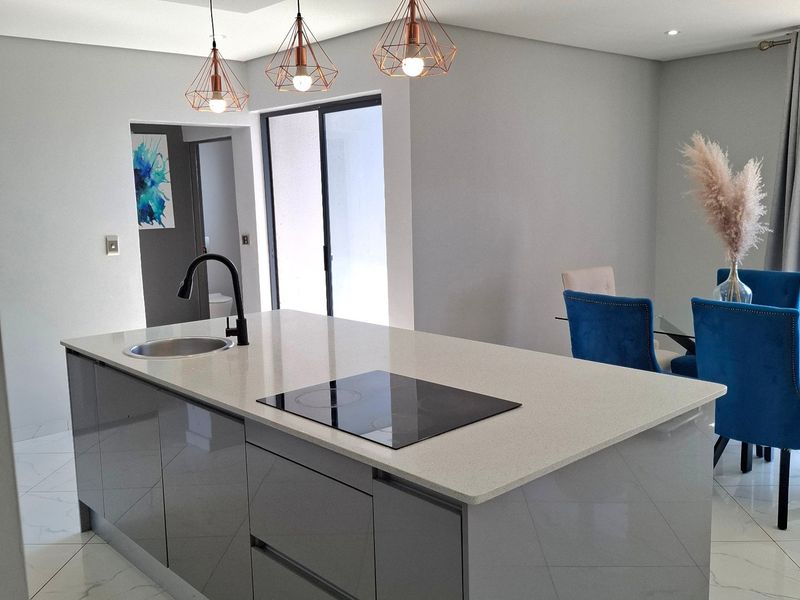 Modern open-plan kitchen featuring a central island with quartz countertops, induction hob, integrated sink, and stylish pendant lighting over marble-look tiled flooring.