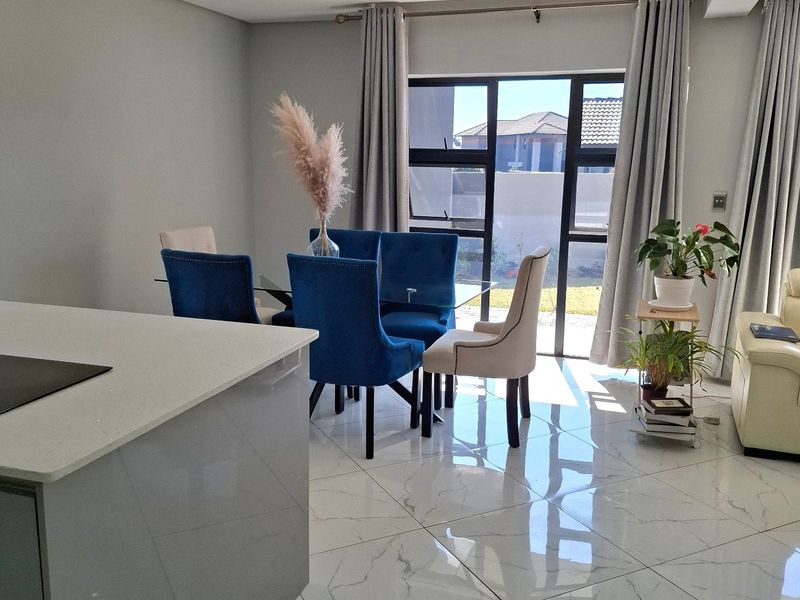 Modern open-plan living and dining area featuring high-gloss marble-look floor tiles, recessed lighting, and large aluminium-framed windows providing natural light.