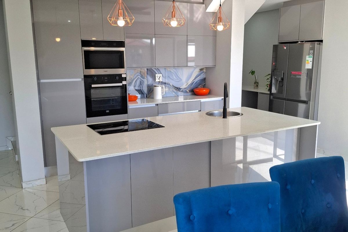 Modern kitchen featuring high-gloss cabinetry, a central island with stone countertops, integrated appliances, and stylish pendant lighting over the workspace.