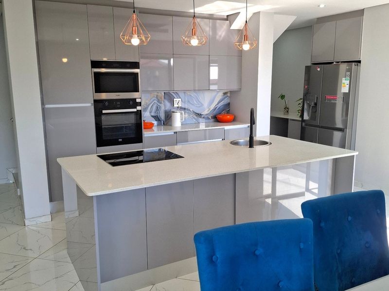 Modern kitchen featuring high-gloss cabinetry, a central island with stone countertops, integrated appliances, and stylish pendant lighting over the workspace.