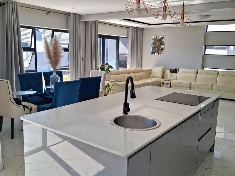 Modern open-plan living area featuring a sleek kitchen island with stone countertops, induction hob, and high-end finishes throughout the bright, spacious interior.