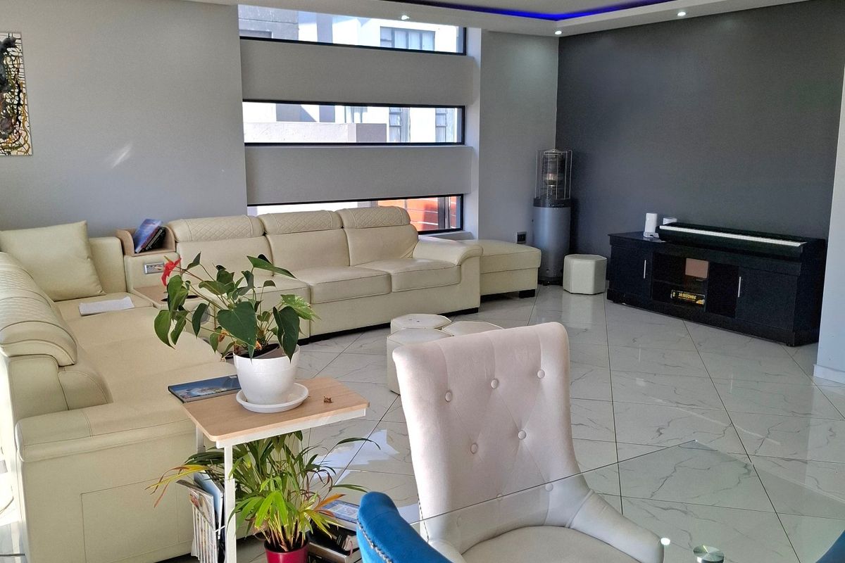 A modern living room featuring polished tiled flooring, recessed ceiling lighting with blue accent cove lighting, and large horizontal windows.