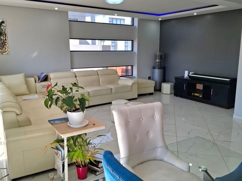 A modern living room featuring polished tiled flooring, recessed ceiling lighting with blue accent cove lighting, and large horizontal windows.