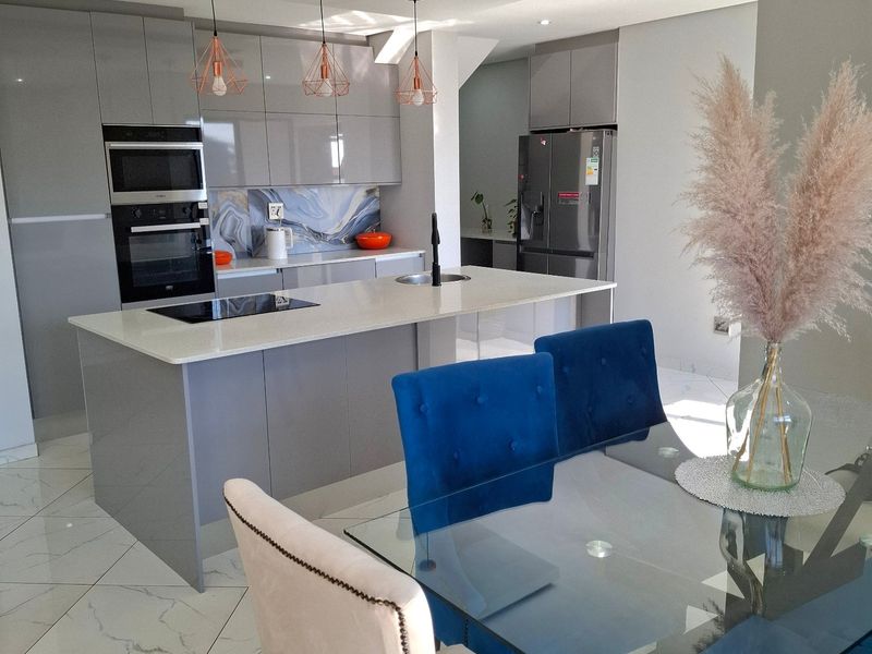 Modern open-plan kitchen featuring high-gloss cabinetry, stone countertops, a central island with integrated appliances, and elegant marble-look floor tiles.