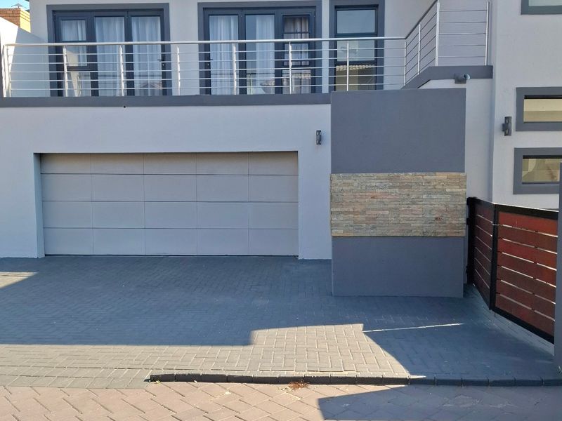Modern front elevation featuring a double garage, paved driveway, and an upper-level balcony with stainless steel railings and stone cladding accents.