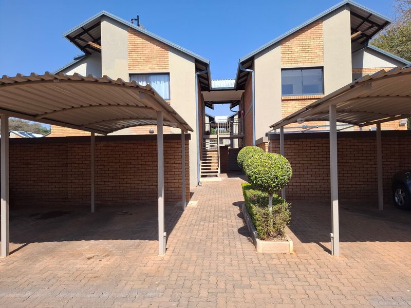 Front view of a townhouse complex featuring covered carports, brick paved driveway, and a central staircase leading to the upper level units.