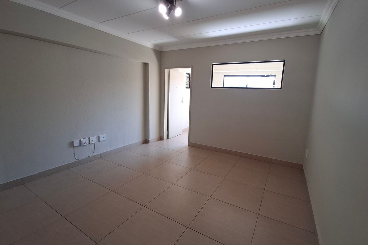 A clean, empty living room featuring neutral tiled flooring, a high-level window, and modern ceiling lighting, providing a versatile blank canvas.