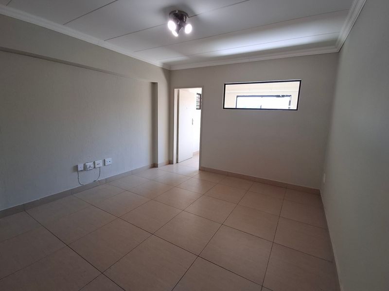 A clean, empty living room featuring neutral tiled flooring, a high-level window, and modern ceiling lighting, providing a versatile blank canvas.