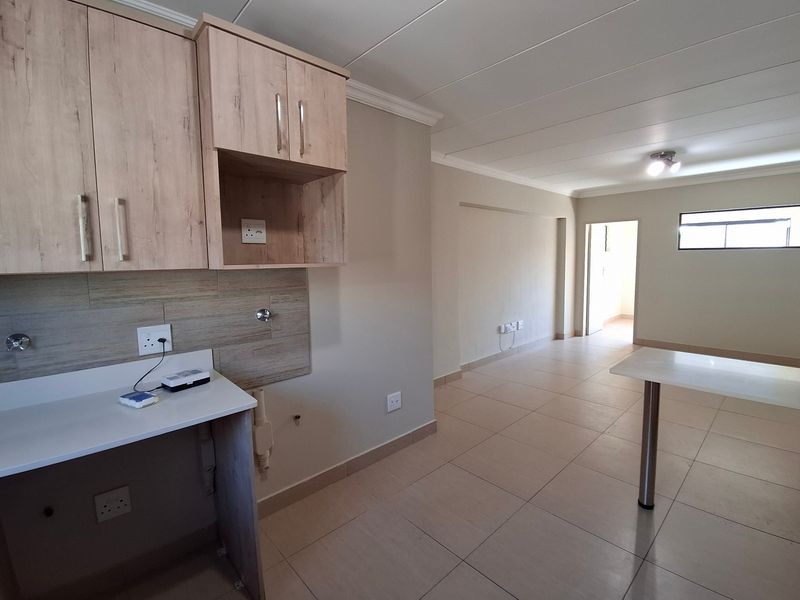 An open-plan living and kitchen area featuring neutral tones, tiled flooring, and built-in cabinetry, offering a clean and versatile space.