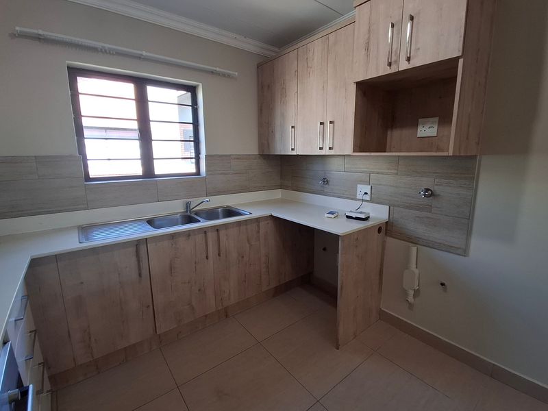 A clean, modern kitchen featuring light wood-look cabinetry, tiled splashbacks, and a stainless steel double sink with dedicated plumbing connections.