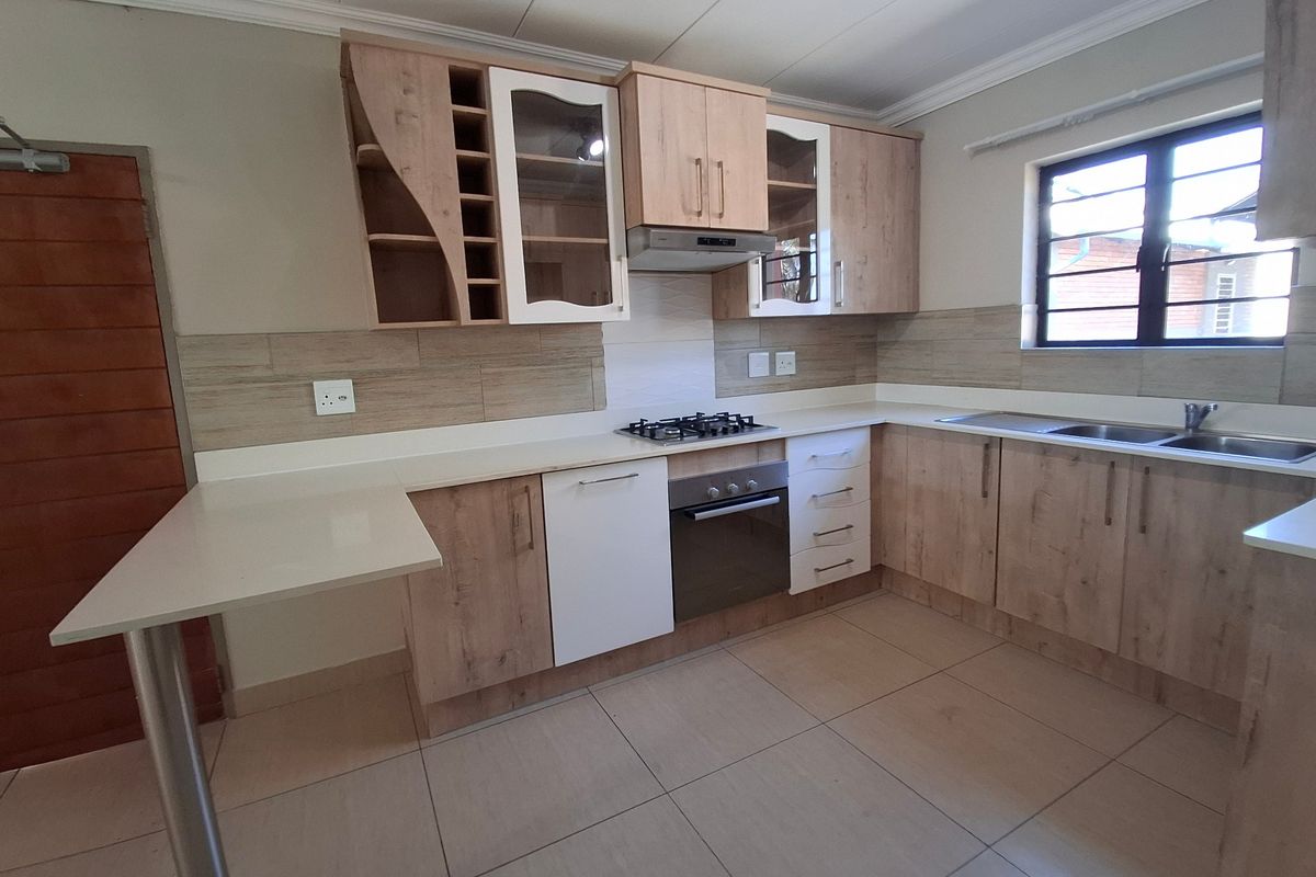 Modern kitchen featuring light wood-tone cabinetry, stone countertops, integrated gas hob, built-in oven, and a convenient breakfast bar area.