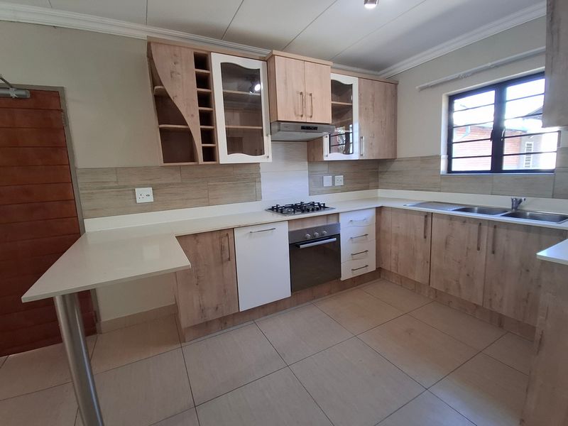 Modern kitchen featuring light wood-tone cabinetry, stone countertops, integrated gas hob, built-in oven, and a convenient breakfast bar area.