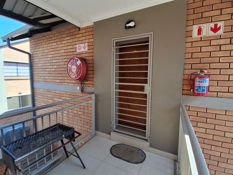 A secure entrance area featuring a metal security gate, brick exterior walls, and essential fire safety equipment including a hose reel and extinguisher.