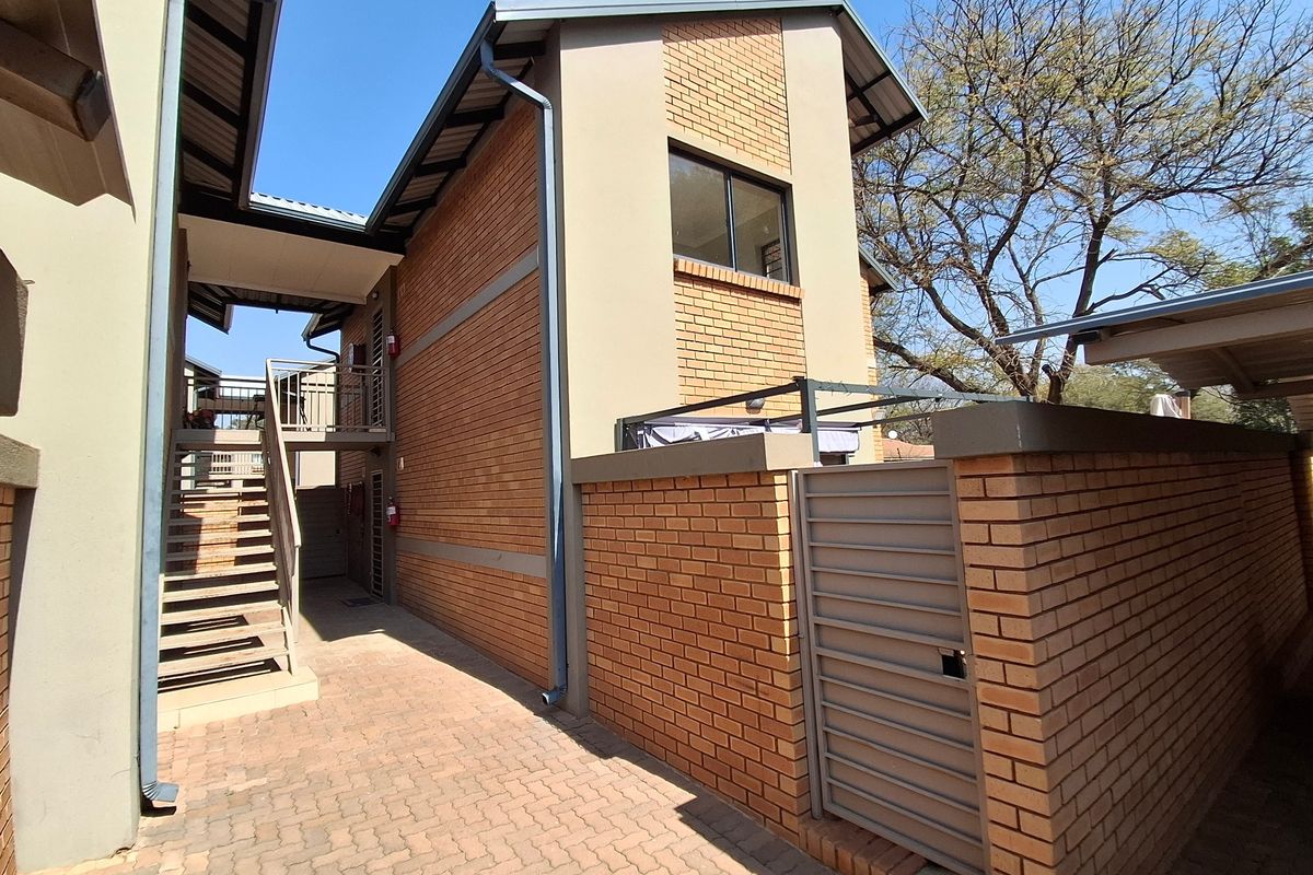 Exterior view of the townhouse rear, featuring a brick facade, paved walkway, and an external metal staircase leading to the upper level.