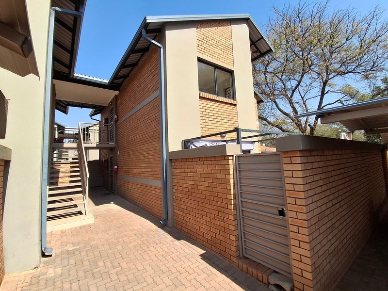 Exterior view of the townhouse rear, featuring a brick facade, paved walkway, and an external metal staircase leading to the upper level.