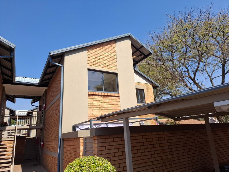 Exterior view of a modern townhouse featuring face brick and plastered finishes, a metal roof, and an integrated carport structure.